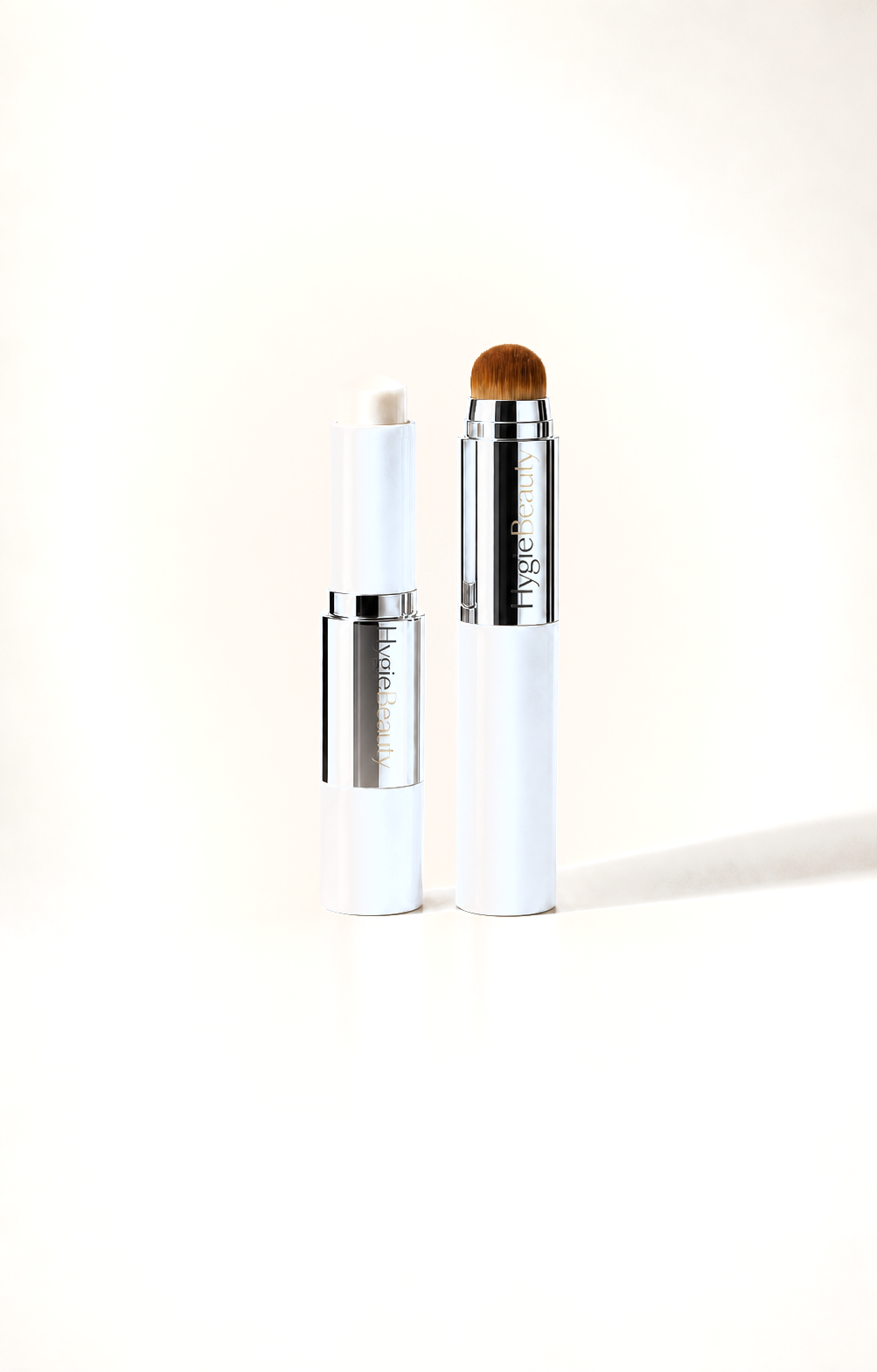 Les deux sticks du fond de teint adaptatif sur fond crème, capuchon blanc et bague argentée gravée HygieBeauty